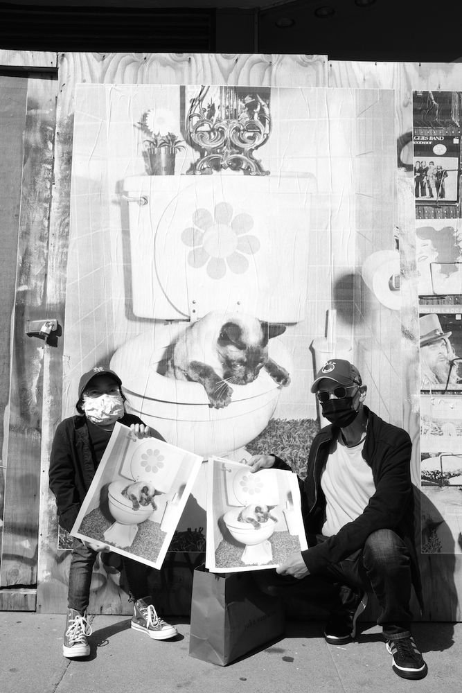 Michael Jang and Jessica Chen in front of The Jangs photo series wheat pasted mural over the boarded up GoodWill storefront, San Francisco, CA 2021