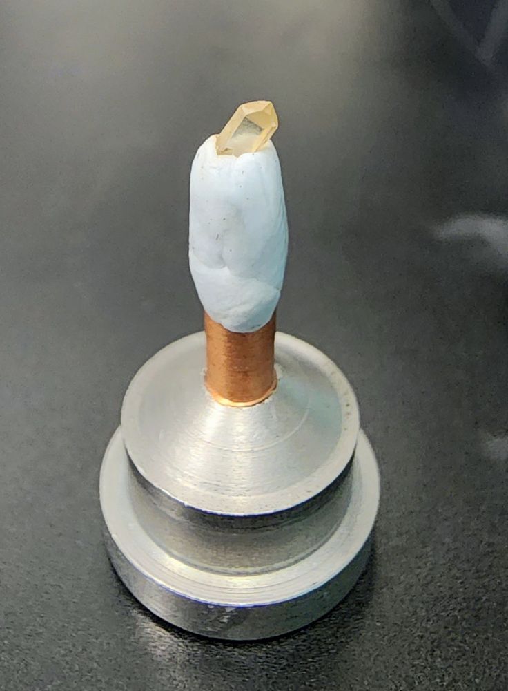 Clear quartz crystal stuck to blutack on a metal pin and base