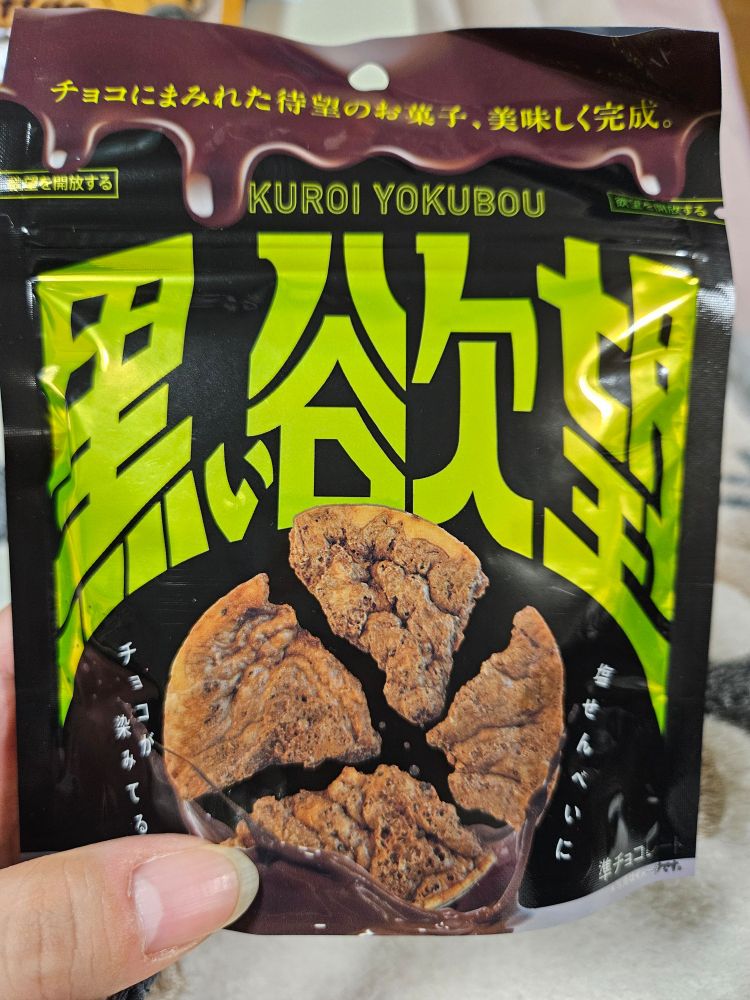 「黒い欲望」という名前のチョコせんべいのお菓子の袋の写真。黒い背景に、ネオングリーンで「黒い欲望」と書かれていて、4つに割れたせんべいの写真が載っている。