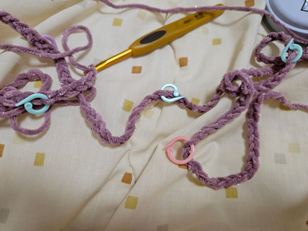 鎖編みされた毛糸の写真。毛糸はくすんだ濃いピンクでラメが入っている。段数マーカーが付いており、黄色い持ち手のかぎ針も写り込んでいる。