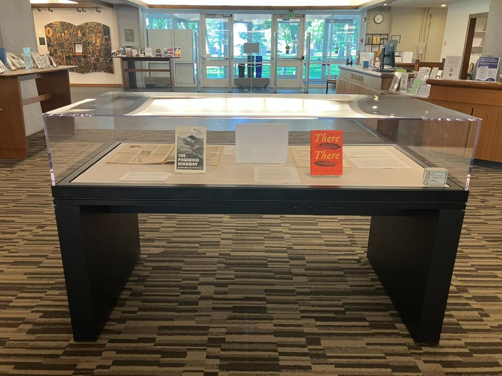 A glass display case in the foyer of a library containing two novels and two historical newspapers
