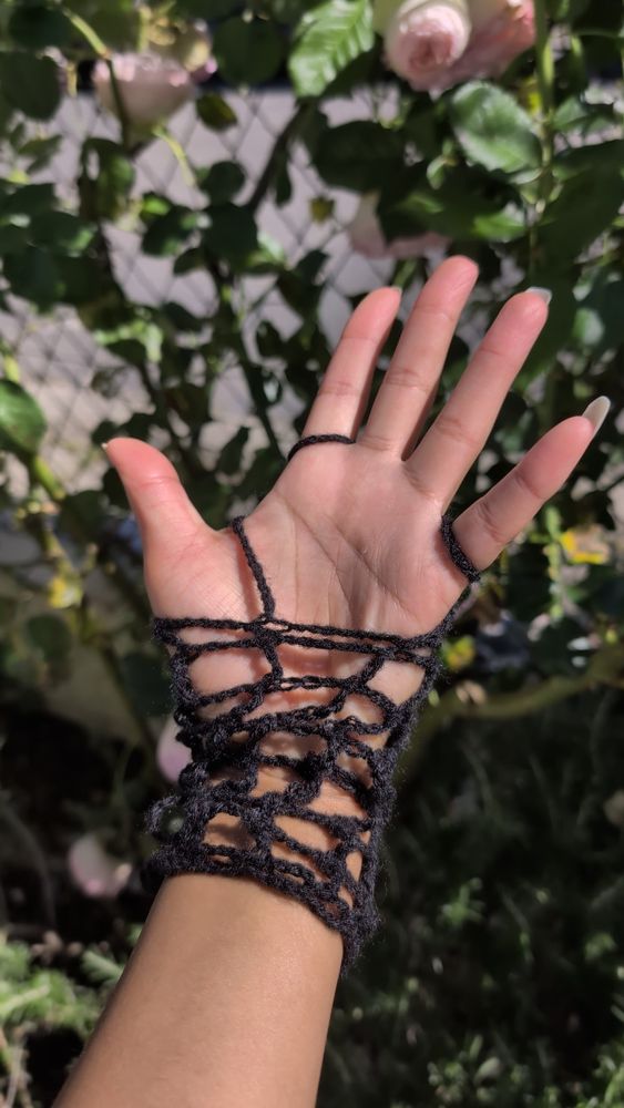 Picture of the left hand's palm wearing a black crochet fishnet glove in front of plants