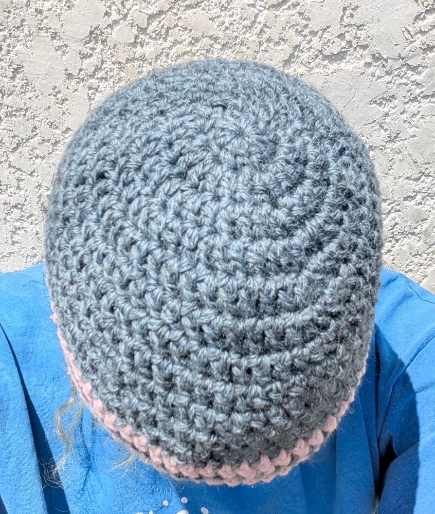 Crocheted blue beanie with a pink stripe and a pink border with pink ties, shown from the top of the beanie 