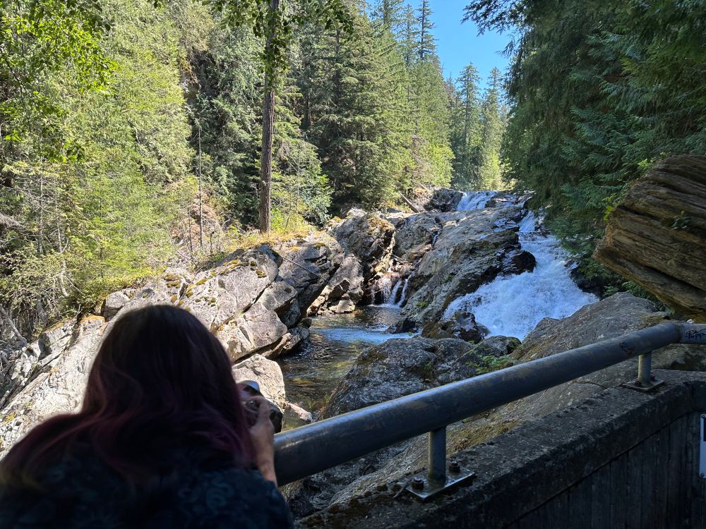 A picture of a woman taking a picture of a waterfall.