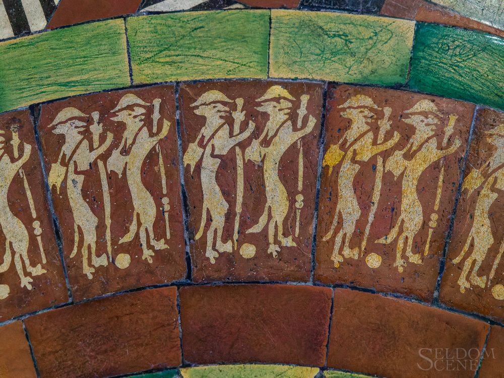 Brown floor tiles are glazed with a procession of stylized foxes dressed as friars.