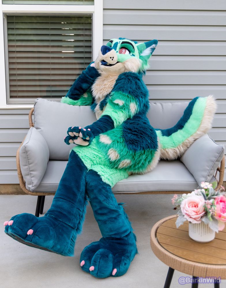 Pretty green fox lady sitting on patio furniture with her legs crossed thinking about sunshine and flowers