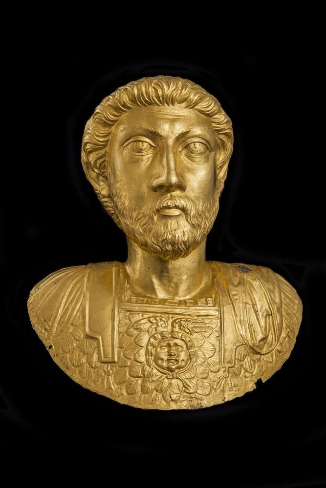 Gold bust of Marcus Aurelius from Avenches. The mustachioed and bearded emperor looks straight ahead with heavy-lidded eyes. An image of the gorgon sits on his breastplate. 