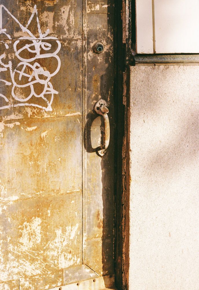 A door in downtown Birmingham. The door is rusty gray. The wall it closes into is sort of quartz pink. 
