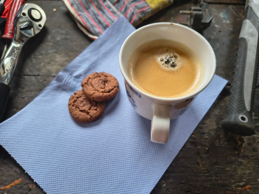 A coffee and two chocolate biscuits on a workbench. 