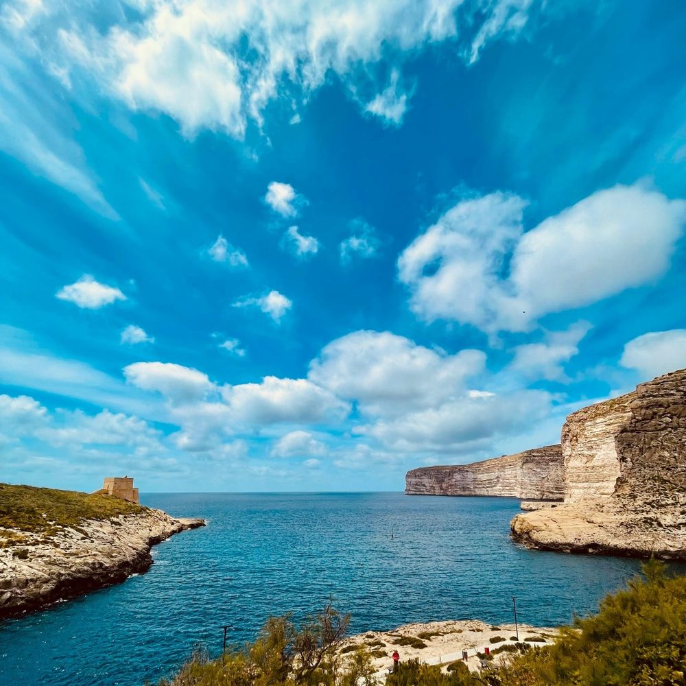 Breathtaking view of blue skies and rocky cliffs meeting the sea in gorgeous Xlendi Bay.