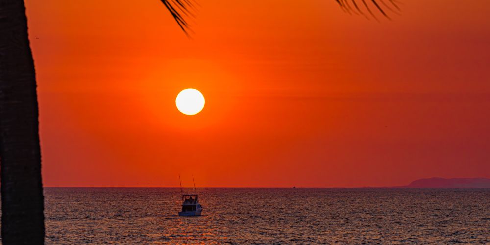 A vibrant sunset over the ocean with a small boat silhouetted on the water.