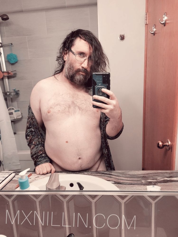 Nillin in a bathroom selfie, their housecoat hang off of their shoulders, exposing their chest and tummy.