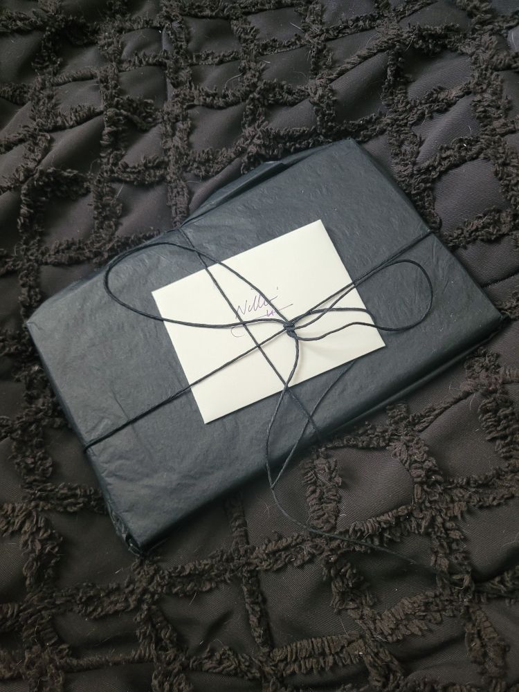 A book wrapped in black parchment paper, with a black string tied around it, and a small white envelope with "Nillin" written on it