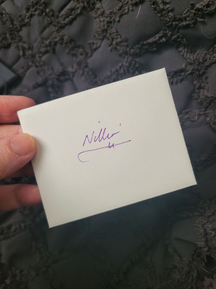 A hand holds a small white envelope with the name "Nillin" written on it.