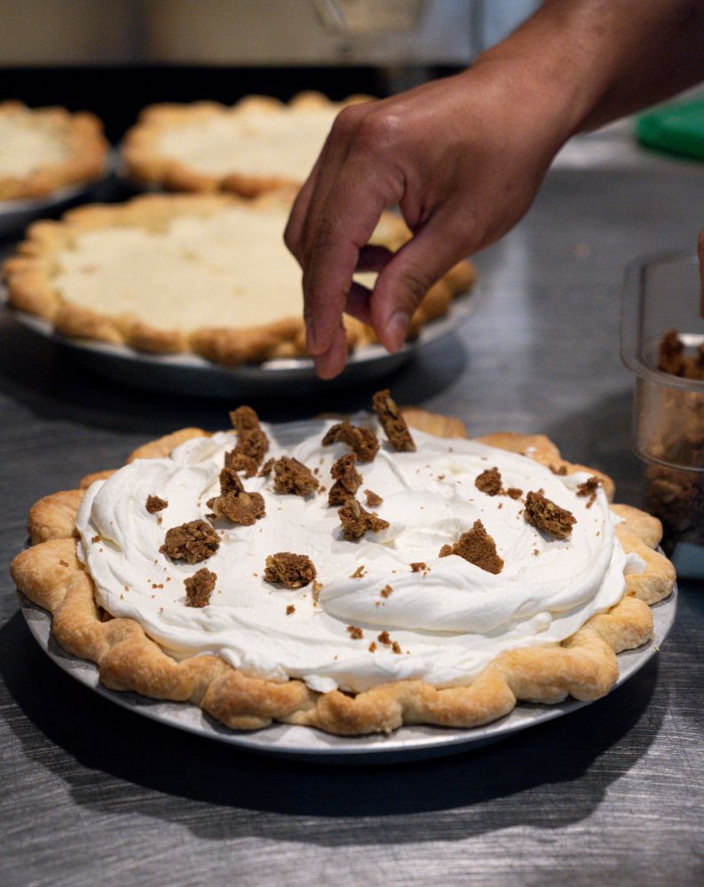 Detail shot of unsliced whole pumpkin pie with cardamon oat crumble being sprinkled on top.