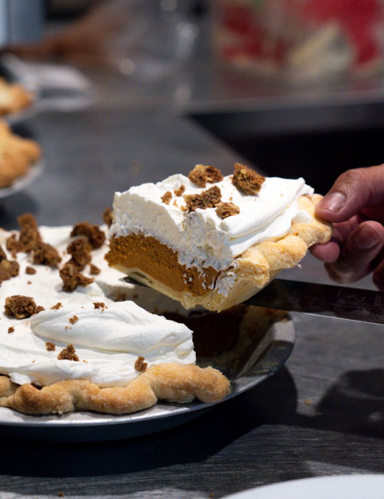 Detail shot of pumpkin pie slice cut out of whole pie. Featuring pumpkin ganache, whipped cream, and cardamon oat crumble.