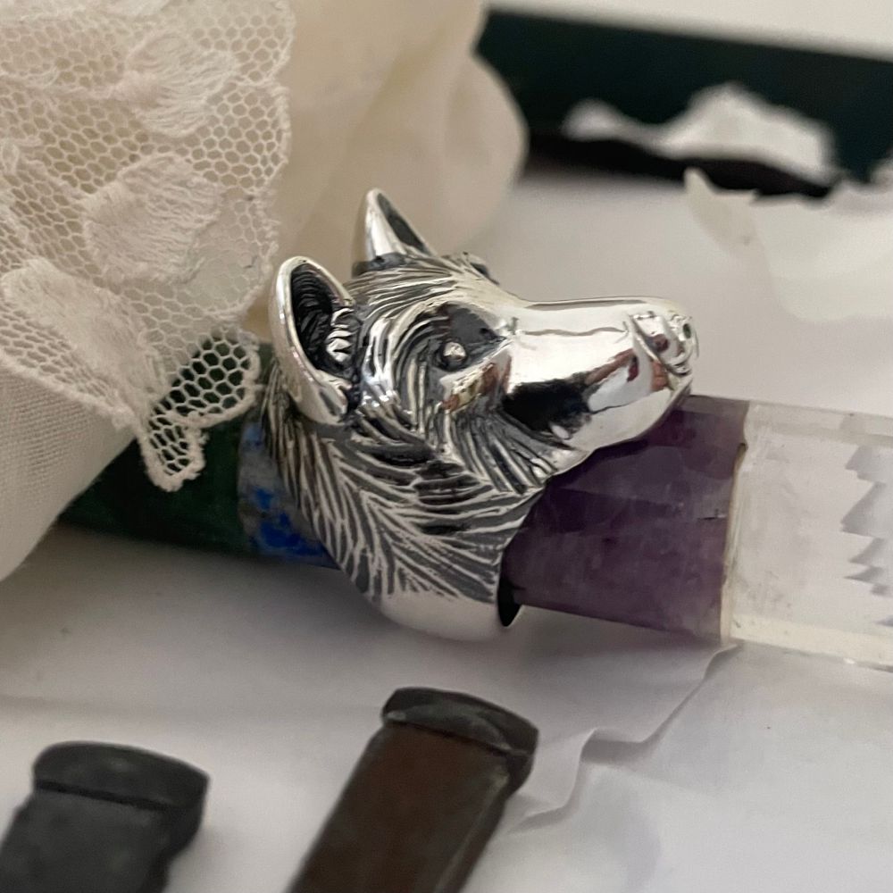 A silver wolf ring sitting on a crystal wand surrounded by white fabric and lace. 