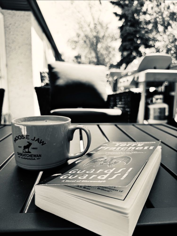 “Guards! Guards!” Book by Terry Pratchett and my coffee on the outdoor table. 