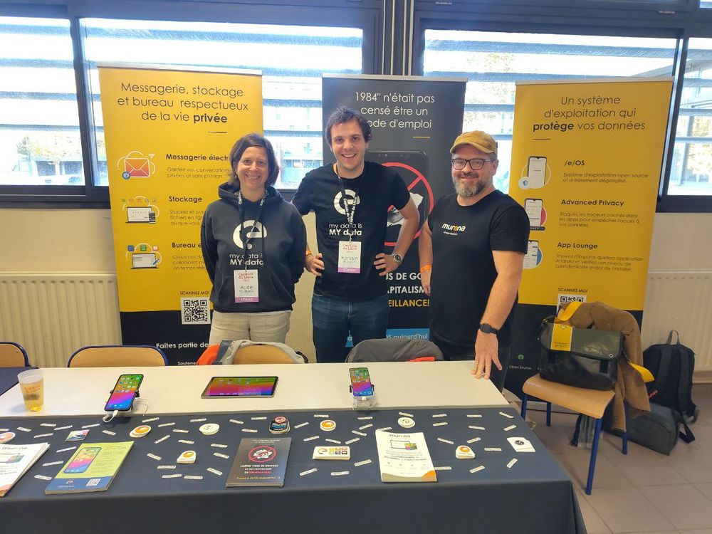 Three of our team members behind the e Foundation booth with 2 smartphones, a tablet, many stickers and flyers