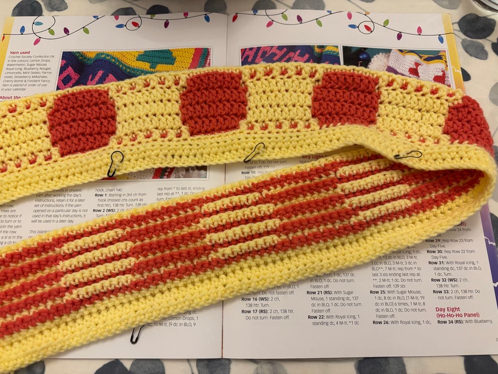 A strip of red and yellow mosaic crochet blanket, folded so you can see the red circles on the right side and the stripes on the wrong side. 