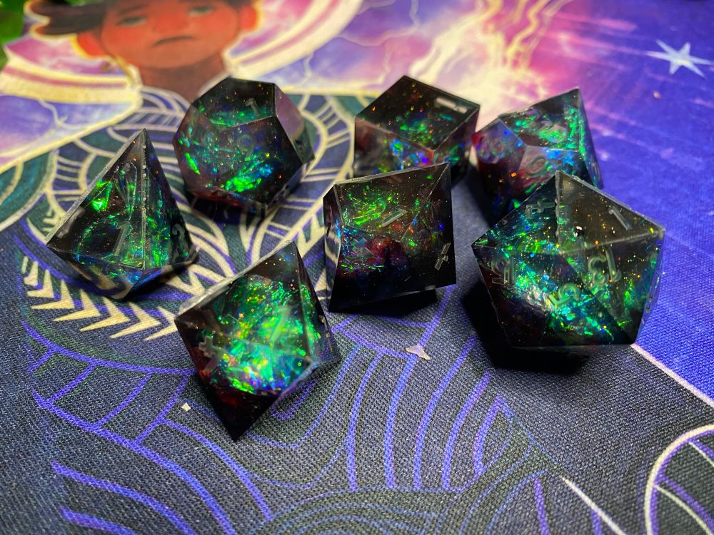 A set of polyhedral dice in black, red and pale blue with green holo foil flashes and hyper holo flake.
