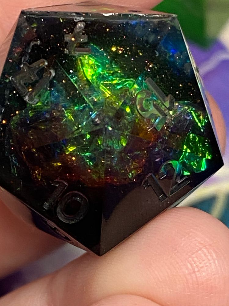 This is a closeup of the d20. It is black, red and has holo foil in it. It also shows the white mica flake that looks like tiny stars, as well as the Nyx pastille glitter that has iridescent facets. 