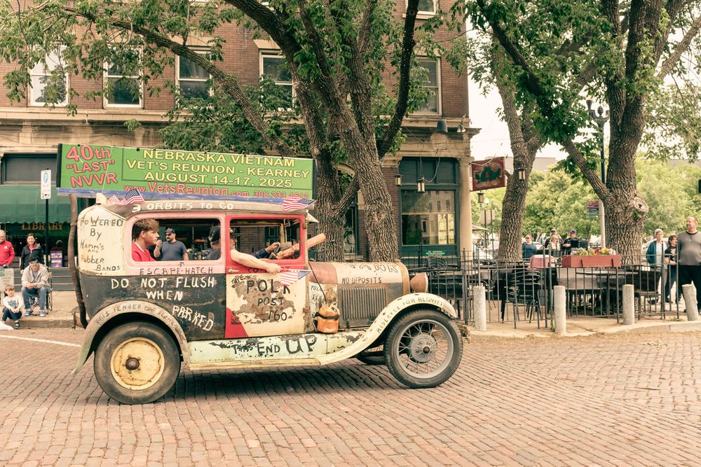 A rattletrap vintage care gaudily painted with "Do Not Flush when Parked," #Powered by Hamm's and Rubber Bands" and advertising the Nebraska Vietnam Vet's Reunion in Kearney August 14-17.