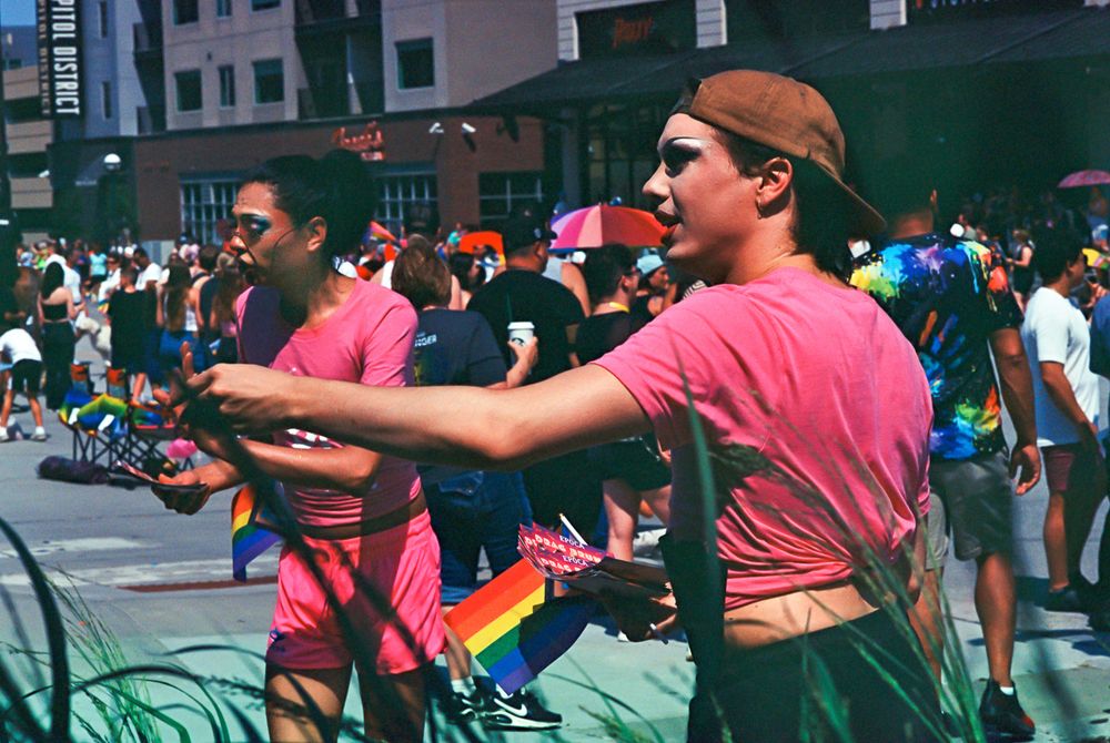 Two participants in Pride Parade hand out flyers. Their faces are as carefully made up as if for Chinese opera.