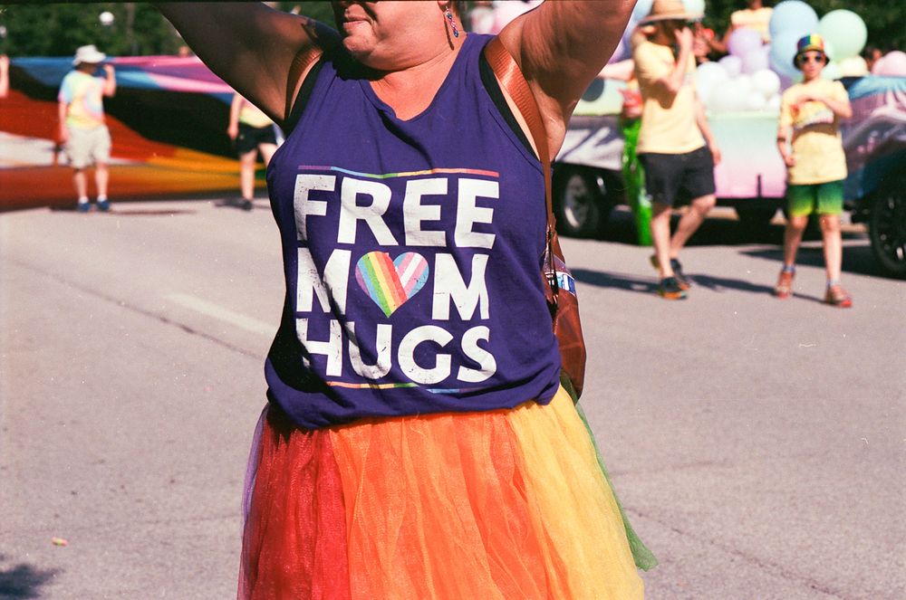 Cropped image of a torso with raised arms wearing a Purple Tee proclaiming "Free Mom Hugs."