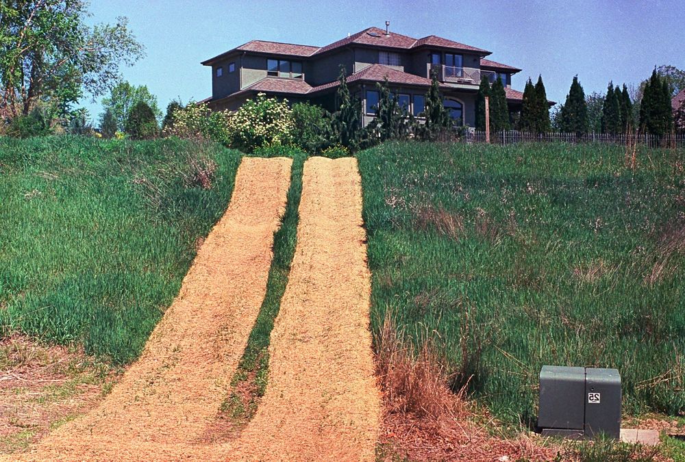 A large house atop a hill. Someone has made a temporary "service road" up to the house with a uniform layer of straw laid down in two swooping parallel lines. (It almost looks like a basket weave.)