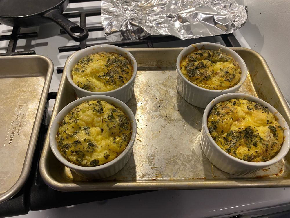 Four crustless mini quiches in ramekins on a quarter pan. All a golden yellow with green flecks from the herbs.