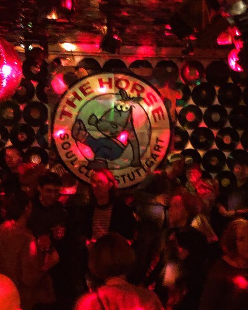 Photo of people dancing on a dancefloor, slightly blurry. Banner on the wall says "THE HORSE. Soul Club Stuttgart" with a cartoon horse in the middle.