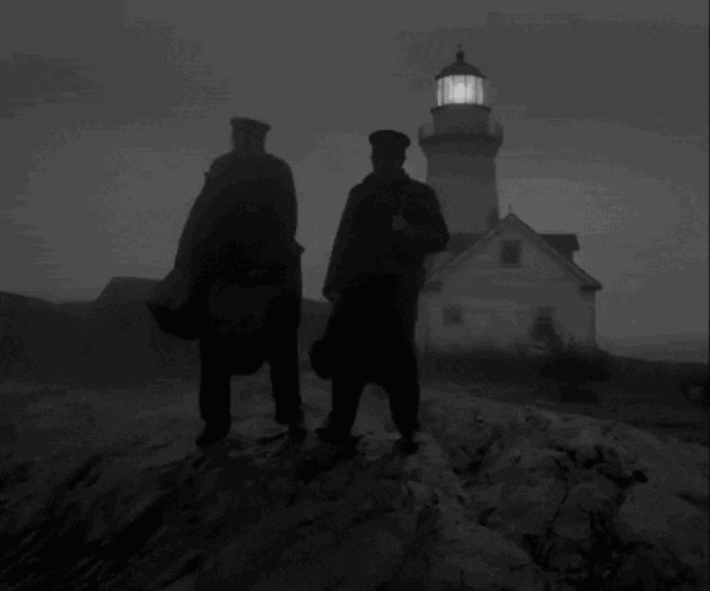 two men standing in front of a lighthouse in the dark .