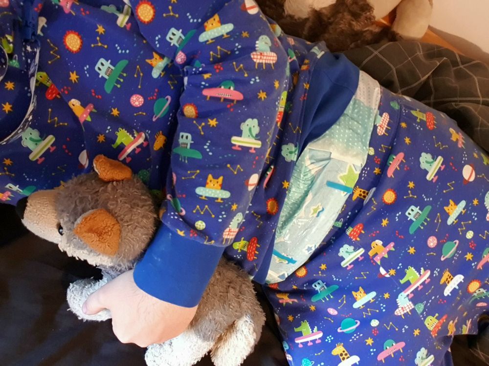 Me wearing space print PJs and hugging a small plush wolf.
A printed diaper shows over my waistband 