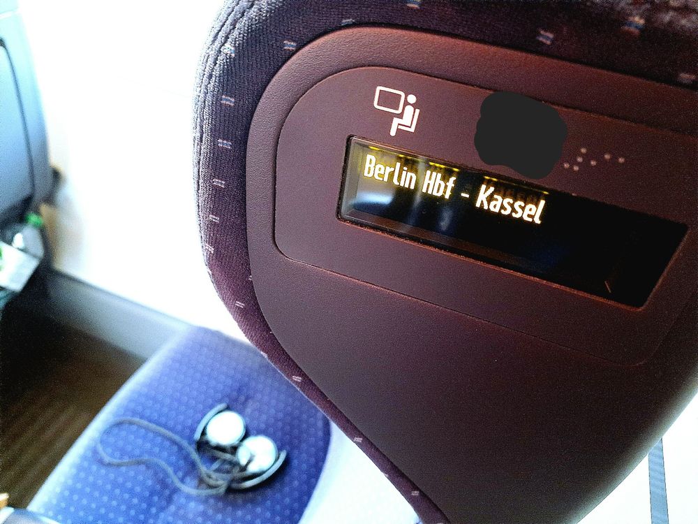 Nahaufnahme des Sitzes mit den Kopfhörern darauf. Fensterplatz, reserviert von Berlin Hauptbahnhof bis Kassel.