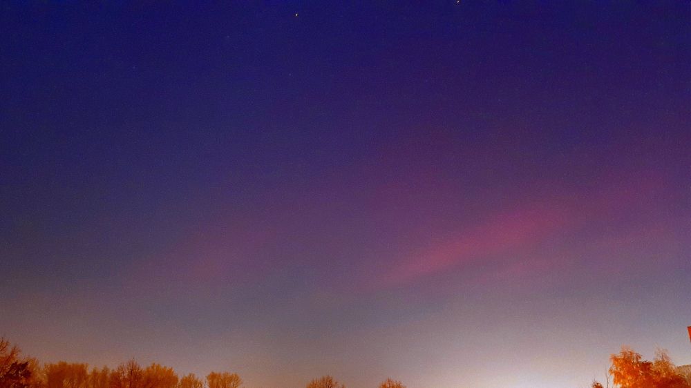 Red northern lights in a foggy night sky with a few stars above the colour structures
