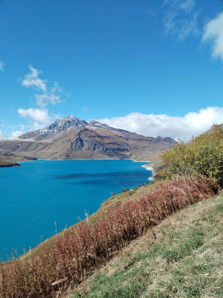 Paesaggio montano soleggiato. Si vede un lago artificiale azzurro. 