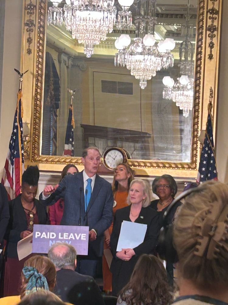 Photo of Senator Wyden at a podium that says “paid leave now” 