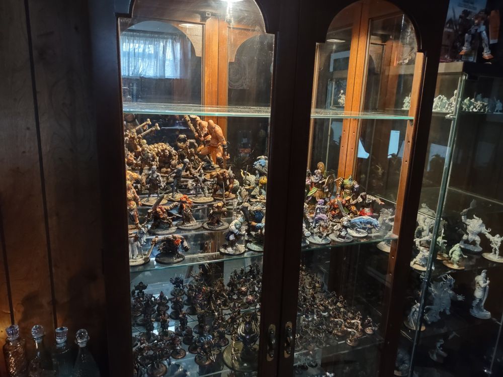 A wide image of a curio cabinet with many miniatures inside, including cryx models and 35 giants of storm, frost, hill, stone and cloud. 