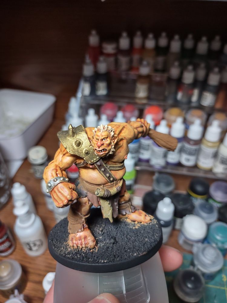Work in progress shot of a hand painted hill giant miniature with blond hair, a fist, and club extended behind him
 