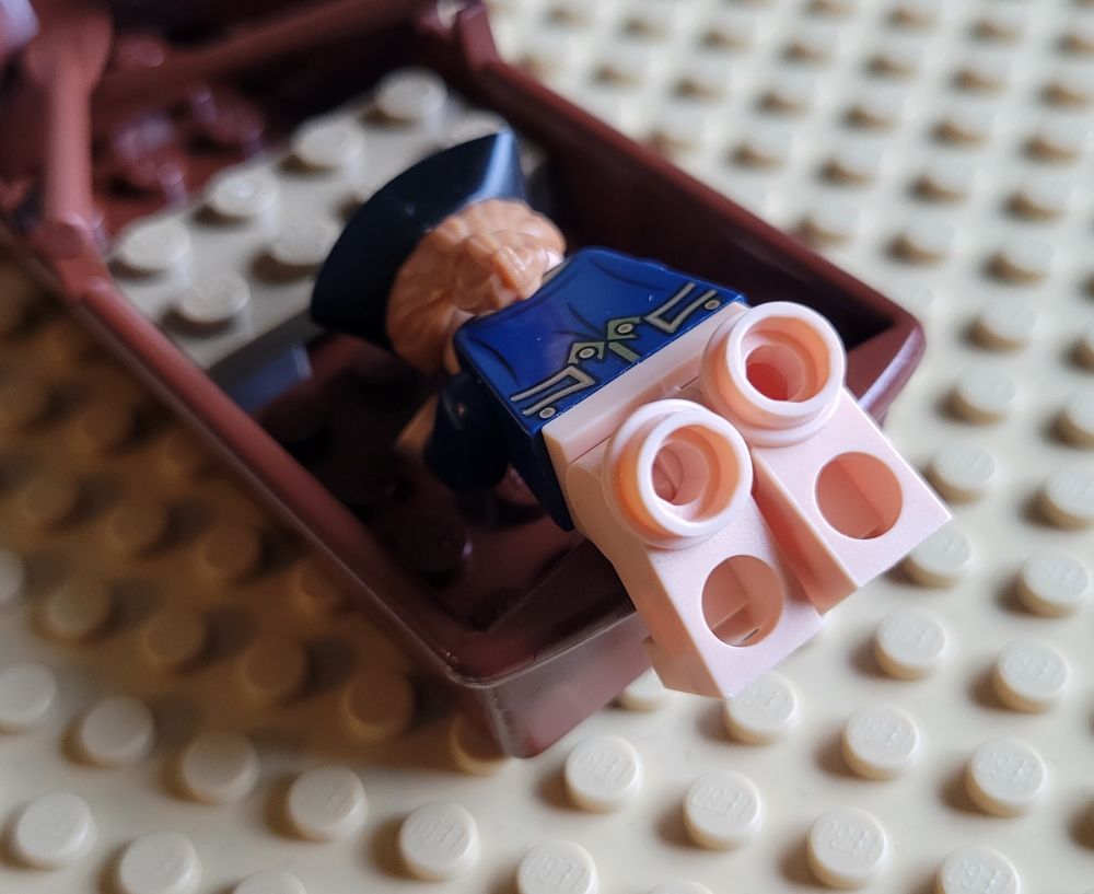 Lego Alex Sherman, half-dressed as a British Navy officer, is draped over the stern of a dinghy. He is showing off his blocky Lego butt to a rabid fan base