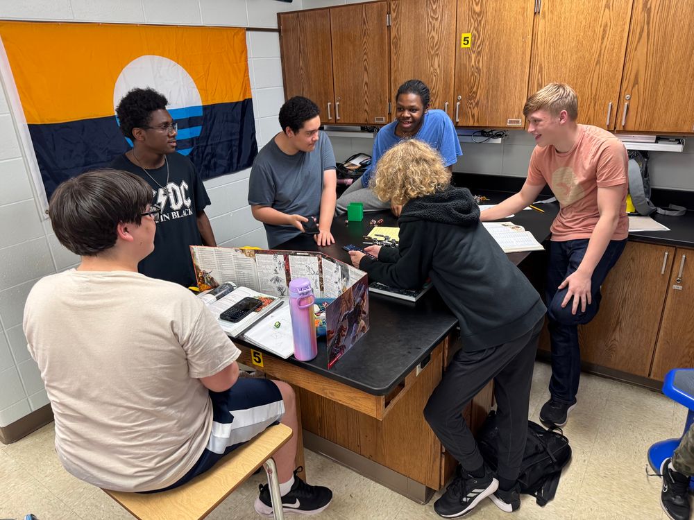 6 high school kids standing around a classroom lab table playing D&D