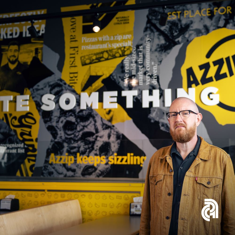 Aaron Tanner standing by his mural at Azzip Pizza.