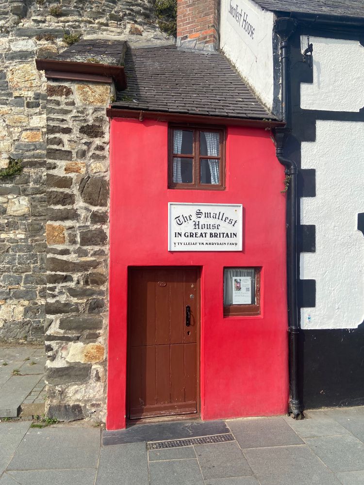 A picture of a comically tiny red house with the plaque saying “The smallest house in Great Britain”