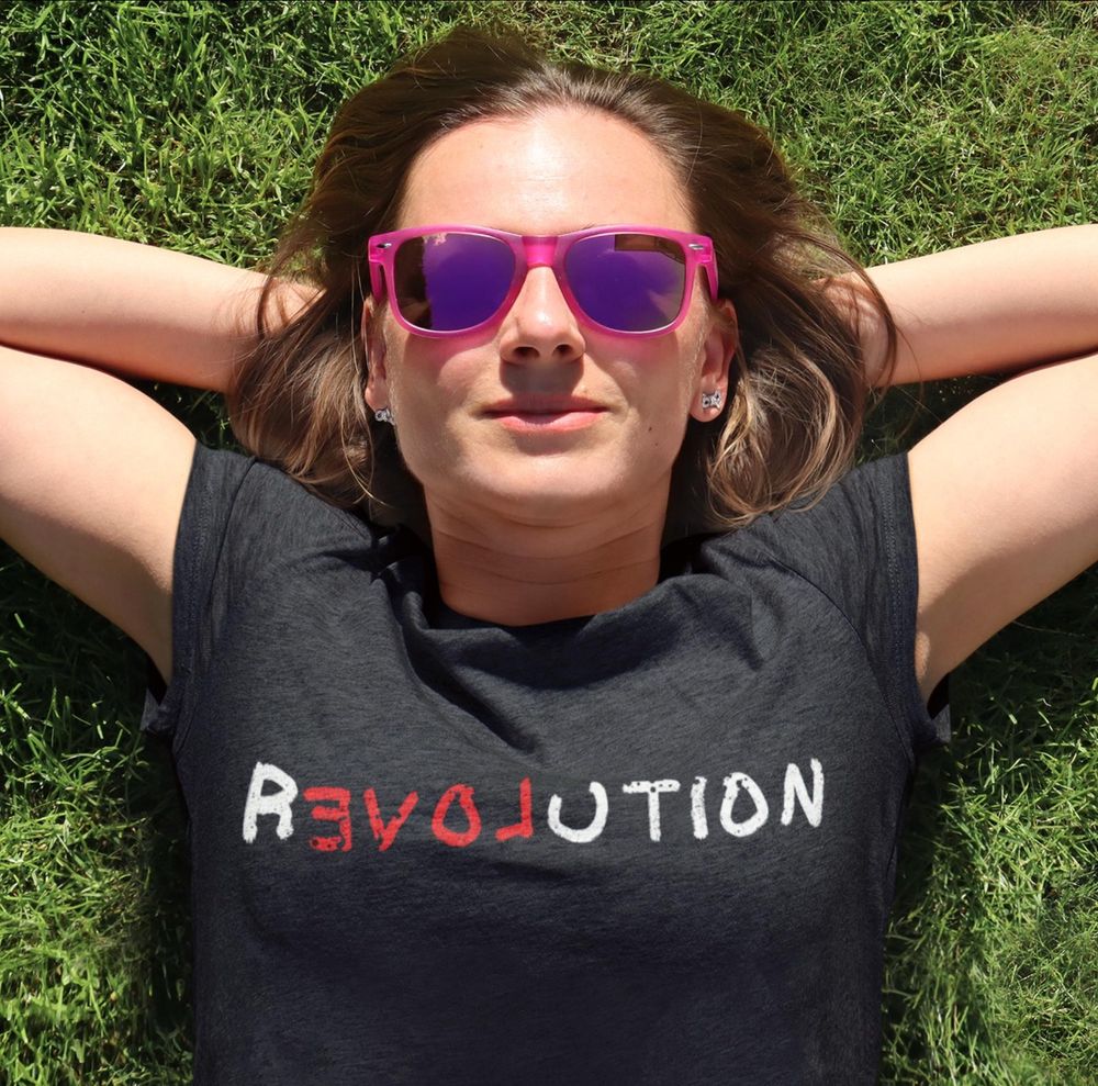 Woman laying on her back in the sun with her hands behind her head wearing a T-shirt that reads Revolution with the EVOL flipped backwards to read LOVE
