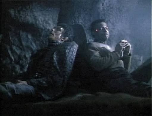 Injured Geordi without his visor sitting in a cave with a Romulan who also is injured 