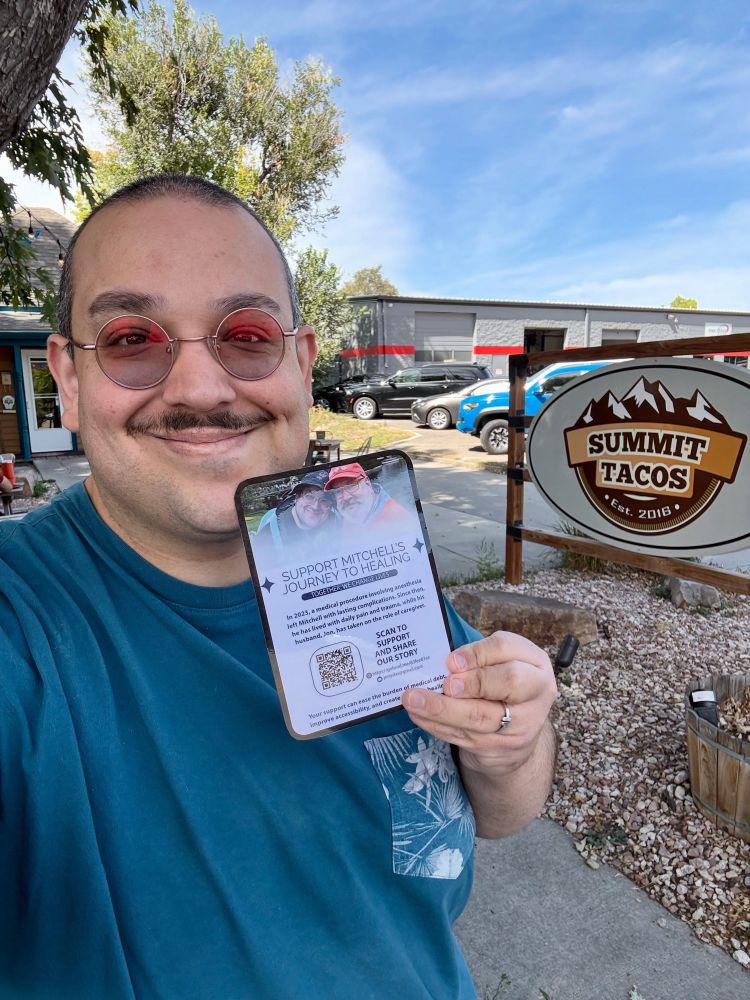 Man standing in front of a restaurant holding up a GoFundMe flyer.
