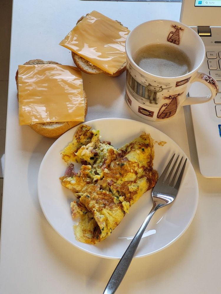 Tasse Kaffee, Käsebrötchen, Rührei mit Speck und Frühlingszwiebeln.