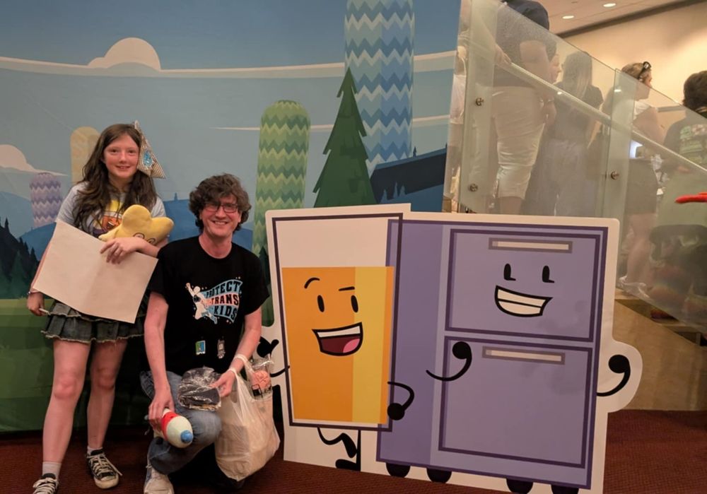 A picture of the kiddo and myself posing next to a cardboard stand of OJ (a glass of orange juice) and Cabby (a filing cabinet) from Inanimate Insanity.