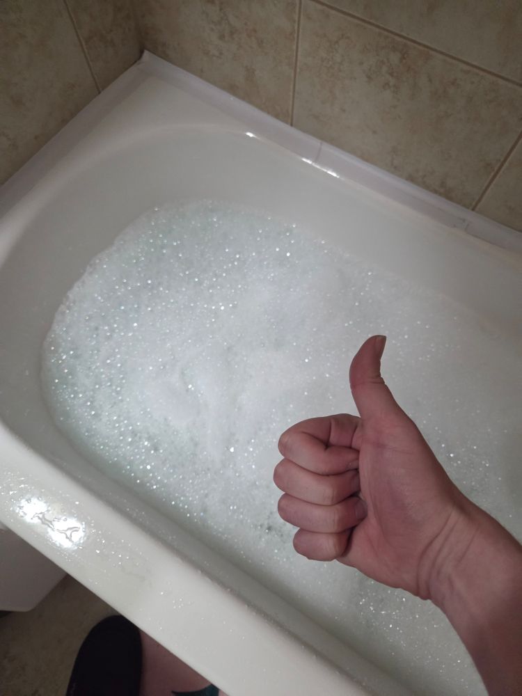 A picture showing a bathtub filled with water and bubbles. In the foreground is my hand giving a thumbs up.